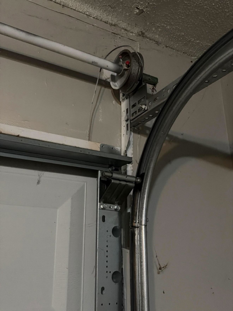 Detail of a garage door track, pulley, and cable system, showing components serviced by J&C Bravo LLC in Cordova, TN.