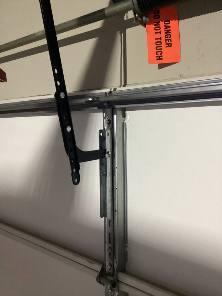 Close-up of a garage door track and spring mechanism with a danger tag, showing work by CCM Overhead Doors in Oklahoma City, OK.