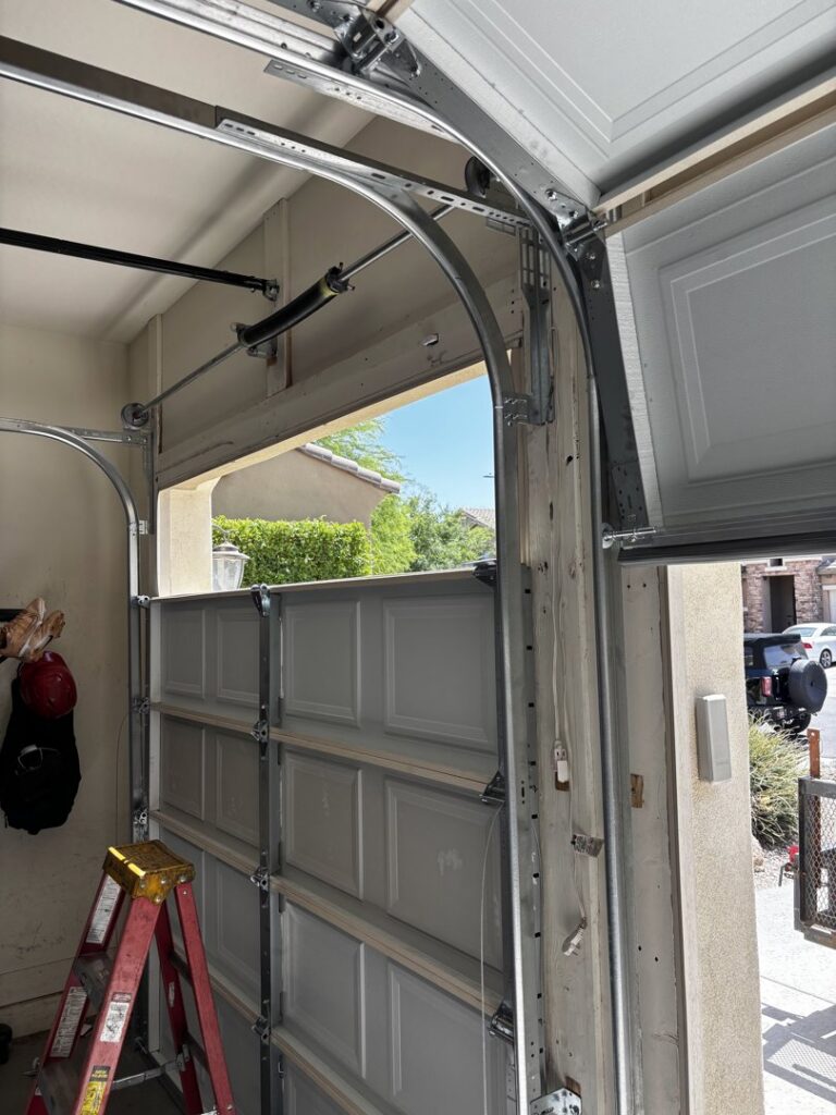 An interior view of a garage door, showing the tracks, springs, and a ladder, indicating a repair or installation job by 101 Garage Doors in Phoenix, AZ.