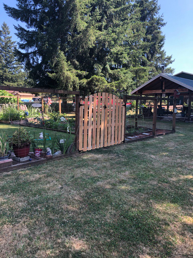 A garden enclosure fence with wire mesh and a wooden gate, built by Faxon Fencing in Corvallis, OR.