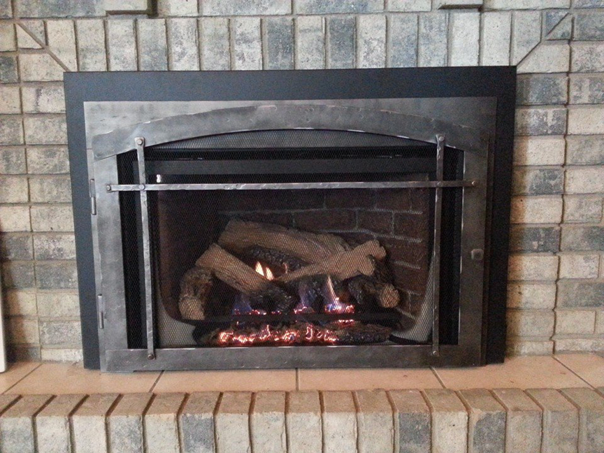 A gas fireplace insert featuring a protective screen and realistic logs, installed by North Central Service, Inc. in Minot, ND.