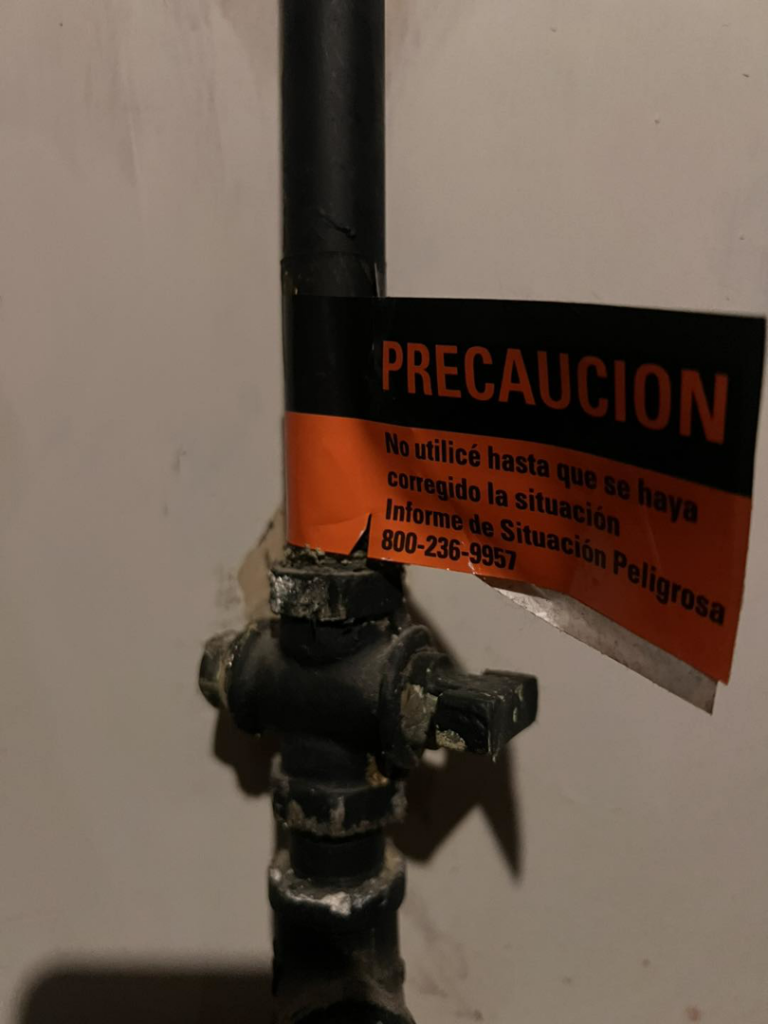 A gas pipe with a 'PRECAUCION' caution tag, indicating a potential issue, at a job site for Basurto's Heating & Cooling in Milwaukee, WI.