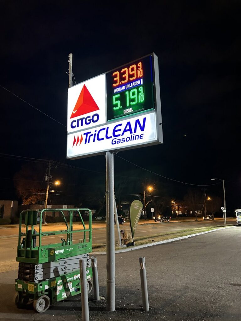 An electrician working on an illuminated gas station sign at night for Parks Electric & Mechanical Co. in Newport News, VA.