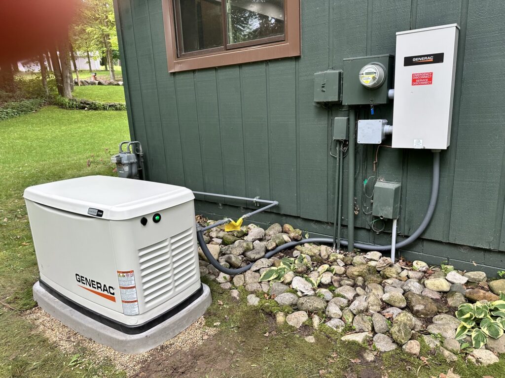 A Generac generator with visible electrical conduit and meter installed next to a house by Great Lakes Power Generation in Williamsburg, MI.
