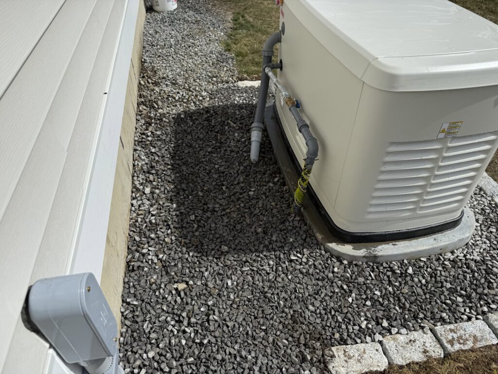 A Generac generator with visible electrical connections installed on a gravel bed by Cason Power Solutions in Lowell, MA