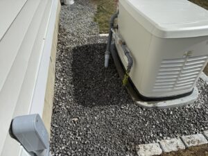 A Generac generator with visible electrical connections installed on a gravel bed by Cason Power Solutions in Lowell, MA