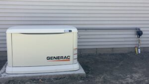 A Generac generator installed on a concrete pad with a gas line connection on the exterior of a house by Great Lakes Power Generation in Williamsburg, MI.