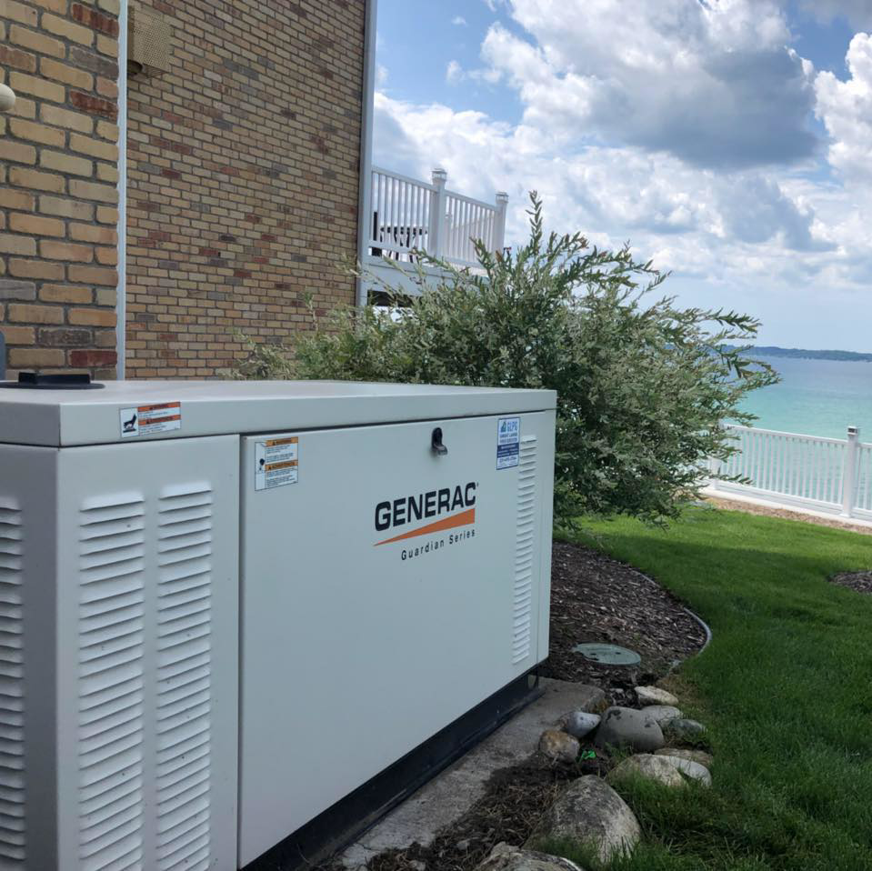 A Generac Guardian Series generator installed next to a brick house by Great Lakes Power Generation in Williamsburg, MI.