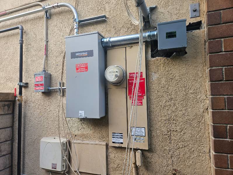 A Generac generator installation with electrical panels and conduits on an exterior wall by Muse Electricians in Los Angeles, CA.