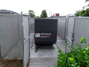 A large Generac industrial power generator securely installed behind a chain-link fence by Varitech, Inc. in Louisville, KY.