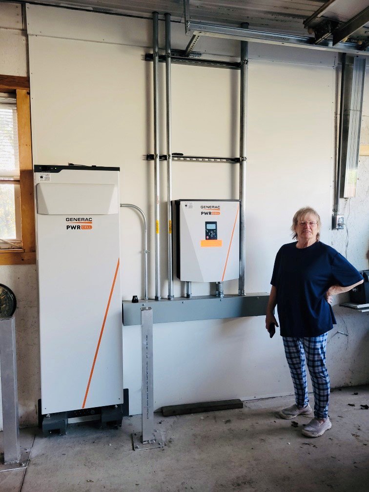 A woman standing next to a Generac PWRcell battery storage and inverter system installed by All Circuit Electrical LLC in Bryant, IN.
