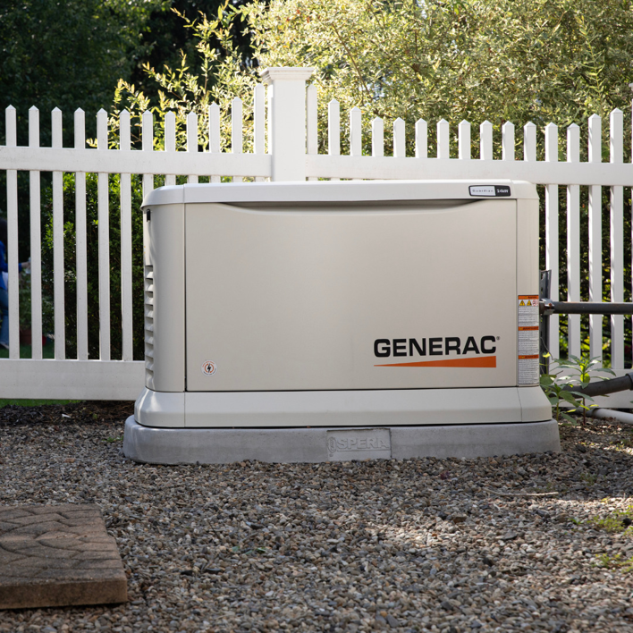 A Generac standby generator professionally installed next to a white picket fence by J&S Power Systems and Small Engine in Laramie, WY.