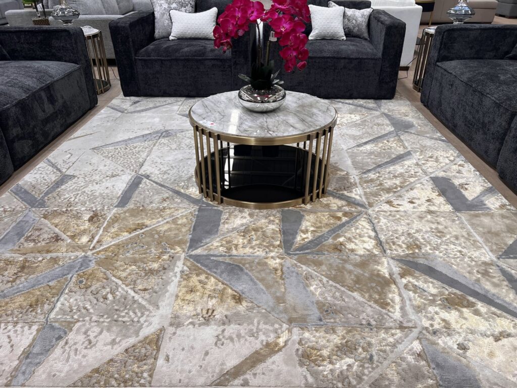 A large geometric patterned rug displayed in a showroom setting with dark sofas at Makymo in Commerce, CA