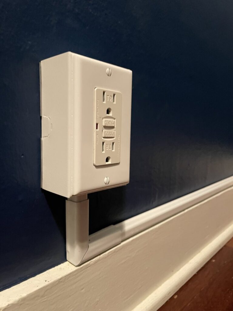 A newly installed GFCI outlet with external conduit on a blue wall by Delatour Electric in Portland, OR.
