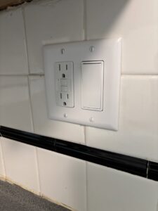 A newly installed GFCI outlet and light switch on a tiled wall, showcasing electrical work by J. Bathe Electric in Saint Charles, MO.