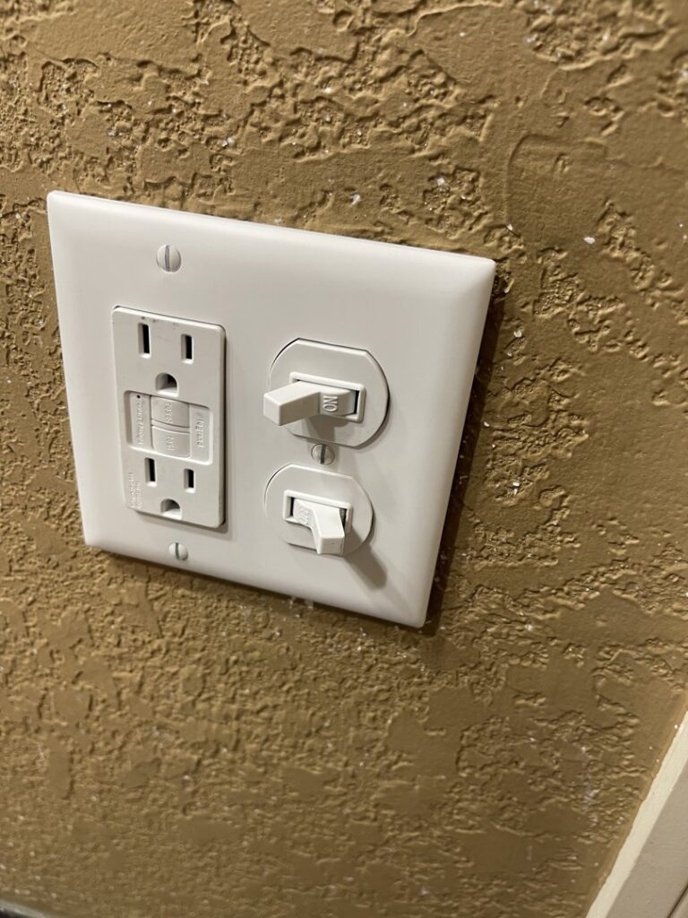 A newly installed GFCI outlet and two light switches on a textured wall by Mister Sparky Kansas City, MO.