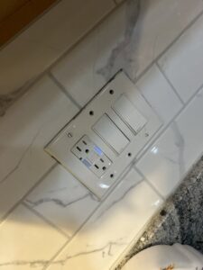 A GFCI outlet and two light switches installed on a tiled kitchen backsplash by Mister Sparky Kansas City, MO.