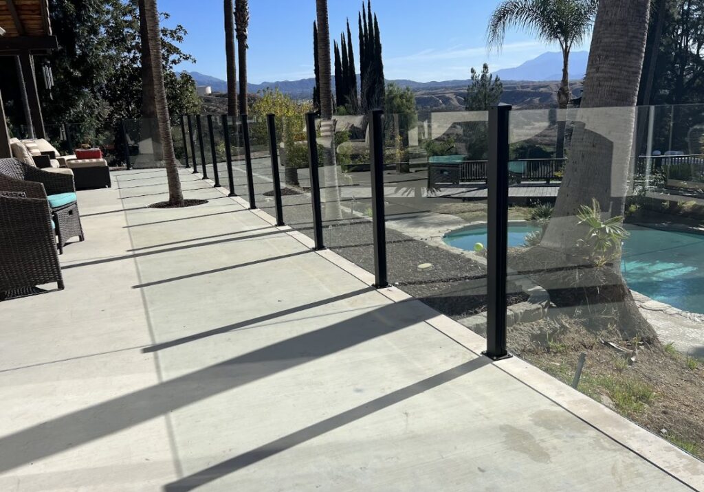 A modern glass panel pool fence with black posts providing safety and clear views, installed by True American Fence Supply and Construction in Anaheim, CA.