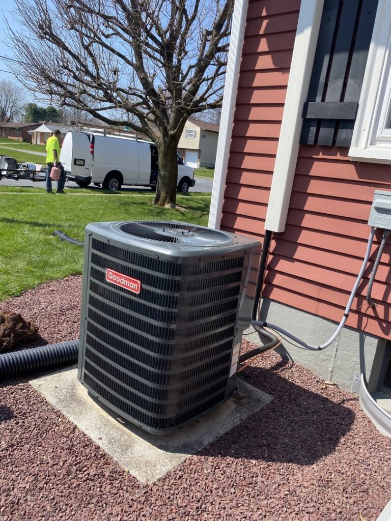 A Goodman outdoor air conditioning condenser unit installed next to a house by Grozier Heating and Air Conditioning, LLC in Allentown, PA.