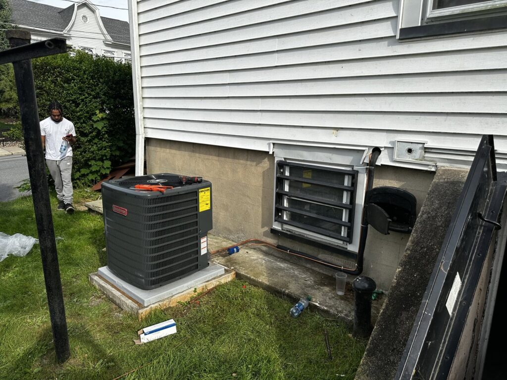 An outdoor Goodman AC condenser unit being installed or serviced next to a house by Alpine Pro Solutions in Allentown, PA.