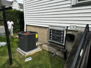 An outdoor Goodman AC condenser unit being installed or serviced next to a house by Alpine Pro Solutions in Allentown, PA.