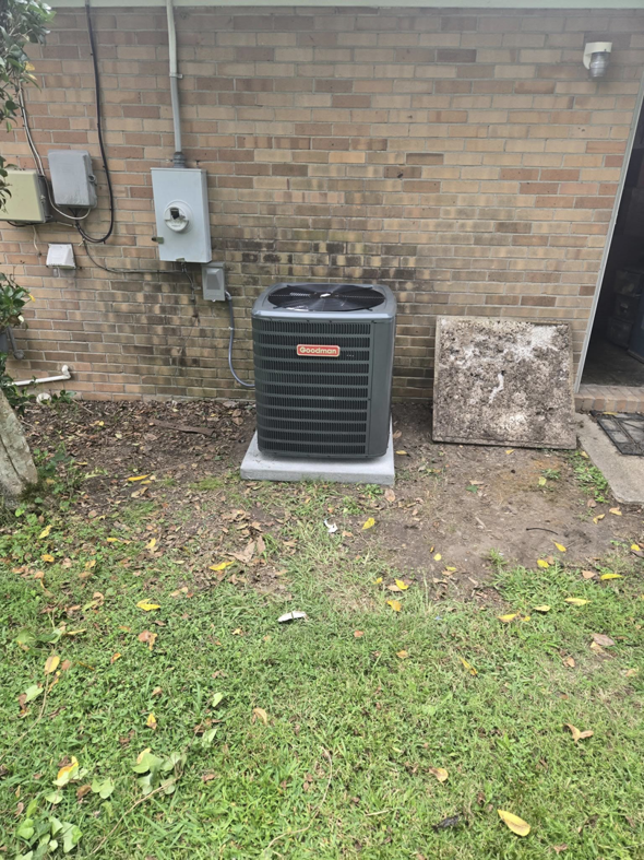 A Goodman brand outdoor AC condenser unit installed next to a brick wall by Jesse's HVAC LLC in Newport News, VA.