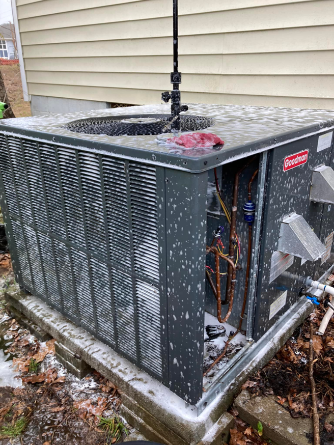 A Goodman outdoor AC unit with its panel removed, showing internal components and cleaning foam during service by Your Angel Heating And Cooling LLC in Cary, NC.