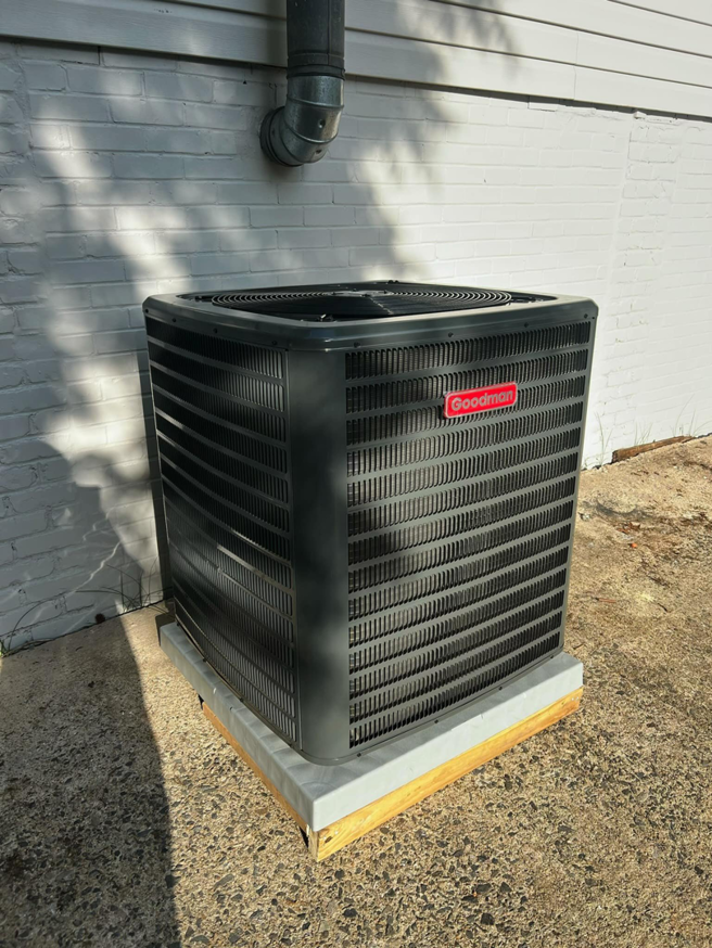 A new Goodman outdoor AC unit installed next to a white house by MTZ Heating and Air Conditioning in Charlotte, NC.