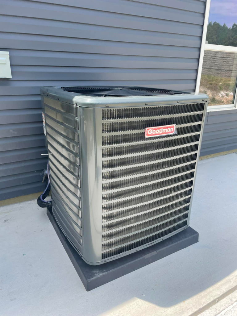 A Goodman outdoor AC unit installed at a new home with gray siding by MTZ Heating and Air Conditioning in Charlotte, NC.
