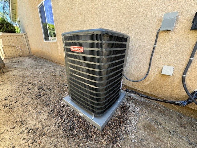 A Goodman brand outdoor HVAC condenser unit installed next to a residential building by Pelican Heating and Air in Carlsbad, CA.