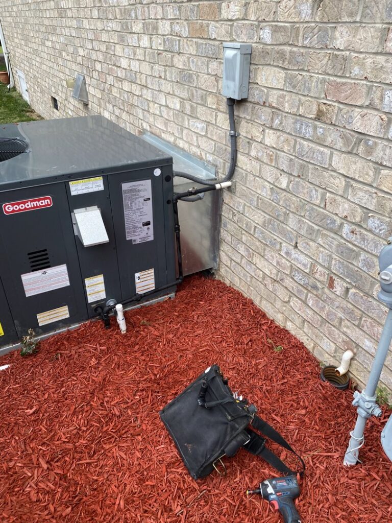 A Goodman outdoor HVAC unit recently installed next to a brick wall, with tools nearby, by Luciano's Air Services in Durham, NC.