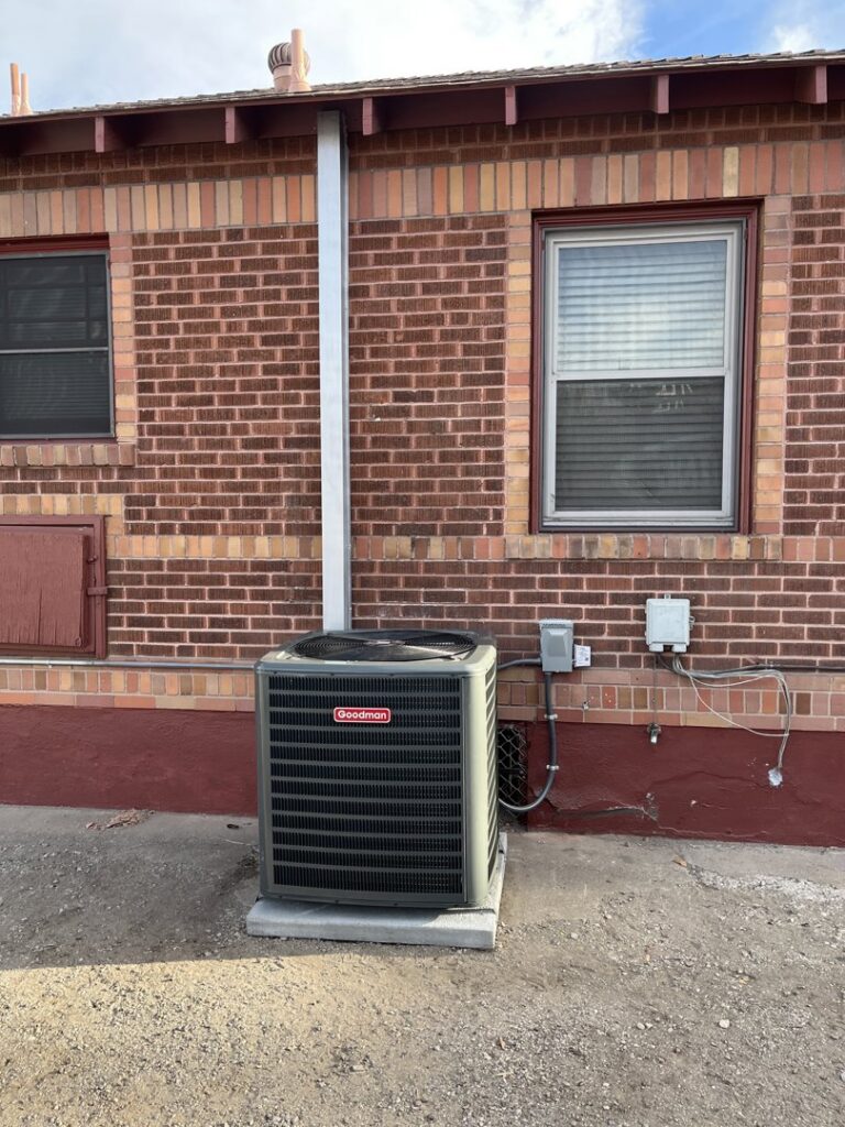 A Goodman outdoor AC unit installed next to a brick building by Nevada Heating Reno in Sparks, NV.