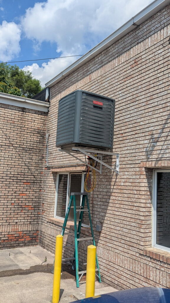 A Goodman outdoor AC unit mounted on a wall bracket, installed by I & M Heating and Cooling in South Bend, IN.