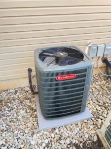 An outdoor Goodman air conditioner system installed on a gravel bed next to a house by American Team Inc in Warminster, PA
