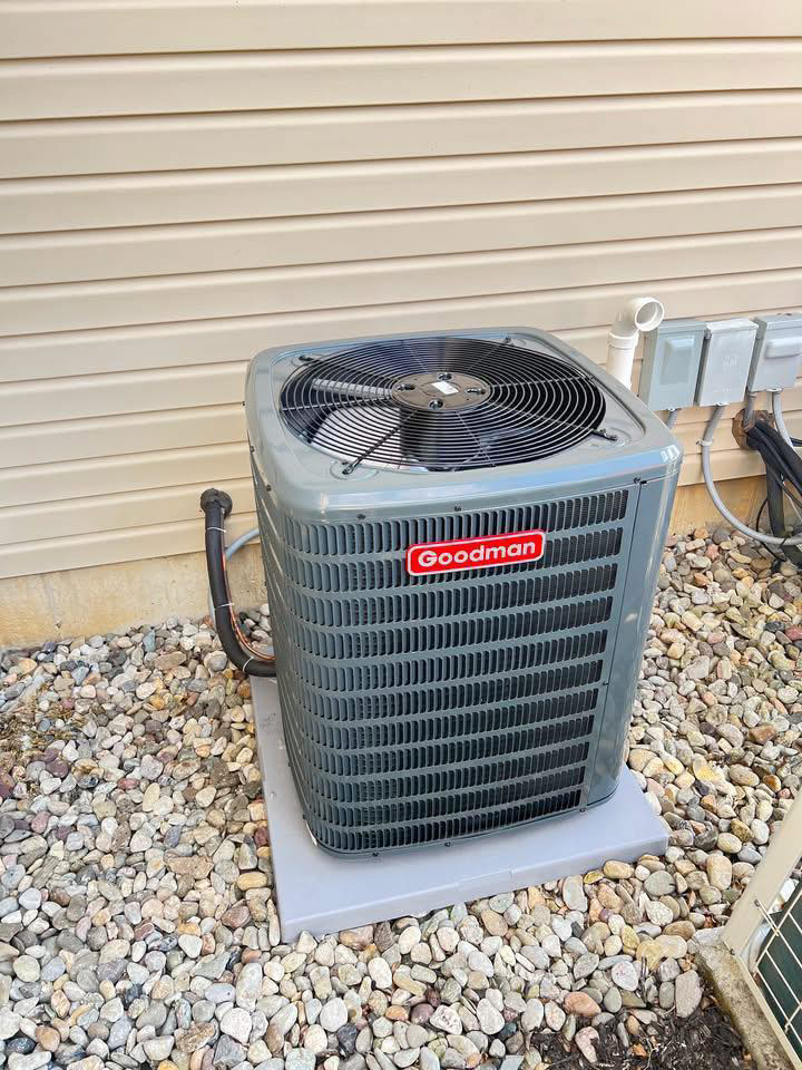 An outdoor Goodman air conditioner system installed on a gravel bed next to a house by American Team Inc in Warminster, PA