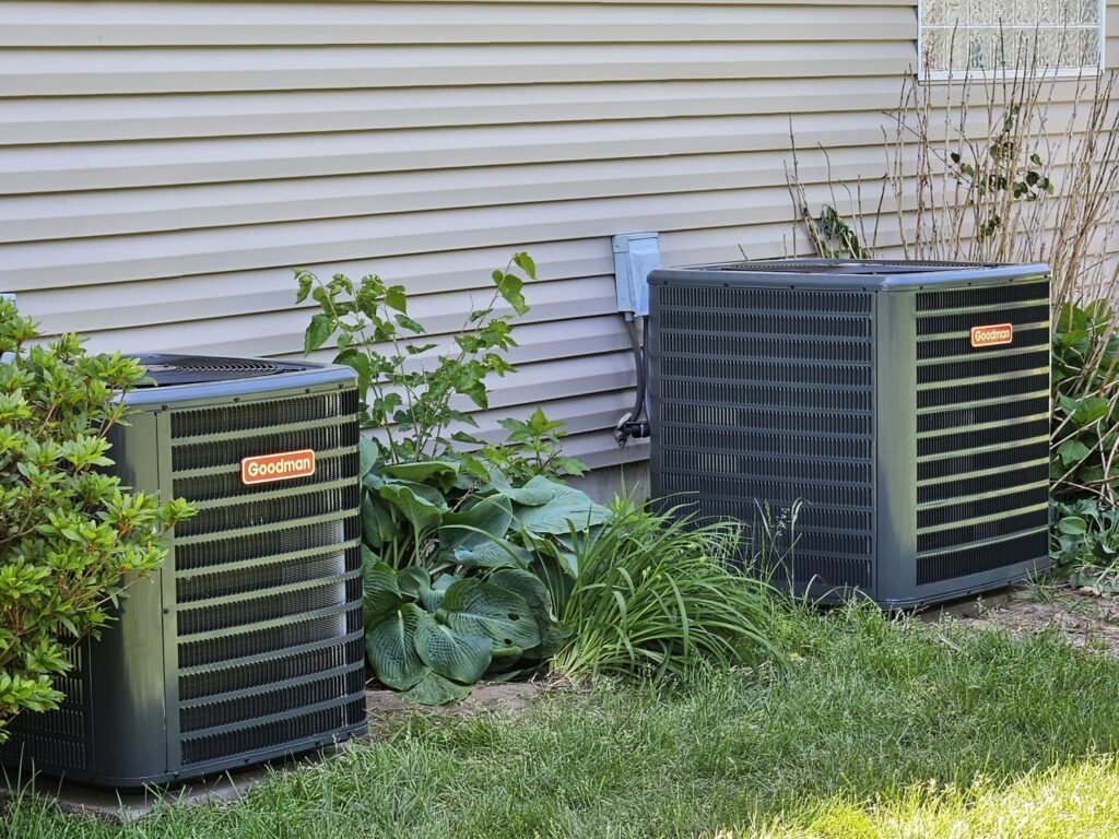 Two Goodman outdoor air conditioning units installed next to a residential building, serviced by TAS Mechanical Services in Kearney, MO.