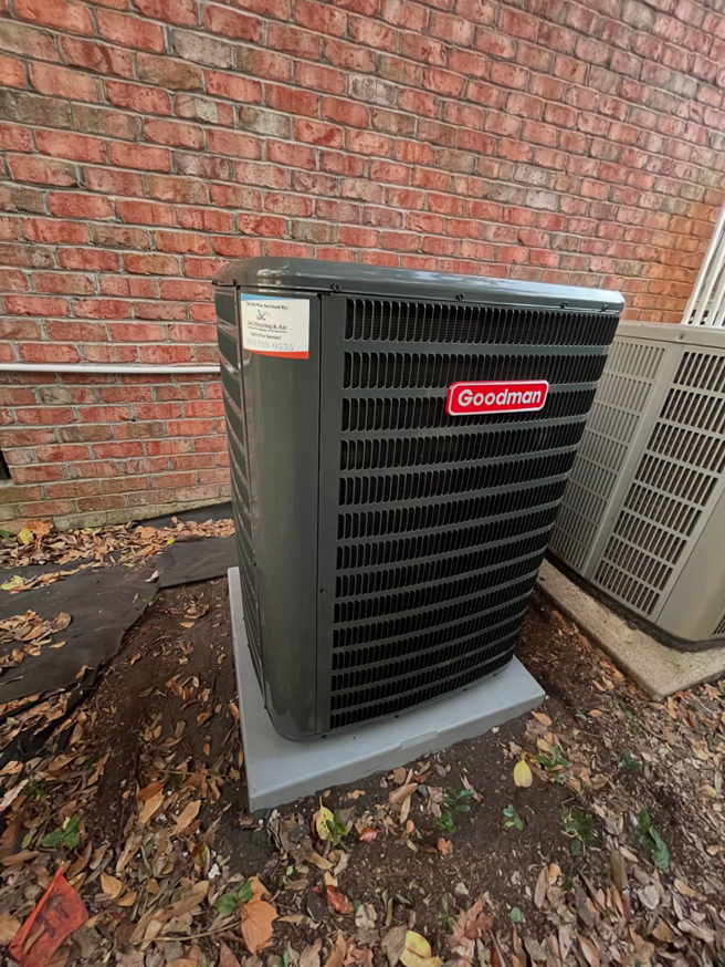 A Goodman outdoor HVAC condenser unit installed next to a brick wall by Joe's Heating & Air Repair LLC in Surf City, NC