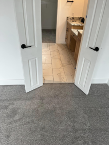 A newly installed gray bedroom carpet leading to a tiled bathroom by Pages Flooring in Springboro, OH.
