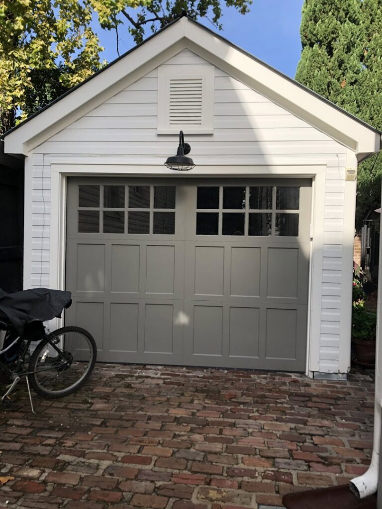 A newly installed gray garage door with windows on a white garage by Precision Garage Door of Charleston in Charleston, SC.