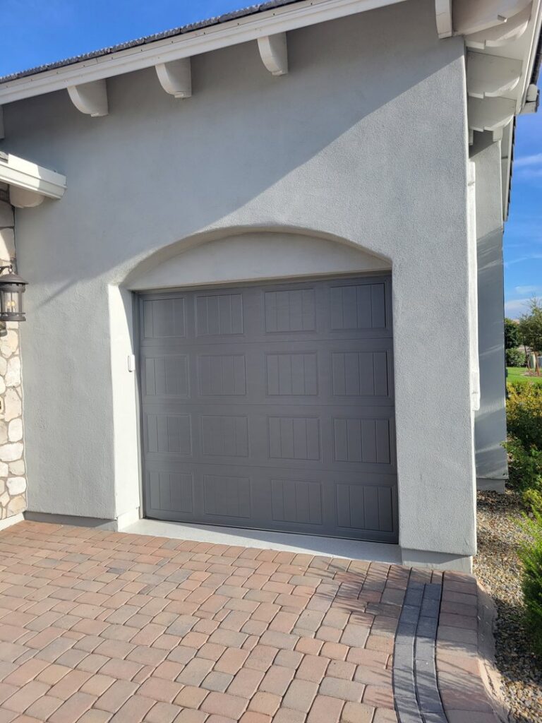 A gray panel garage door installed within an elegant arched opening, a service from JT's Overhead Doors in Gilbert, AZ.