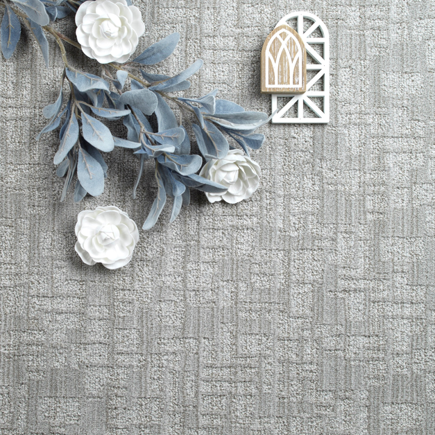 A close-up view of a gray patterned carpet sample with decorative elements from Carpet World Bismarck in Bismarck, ND.