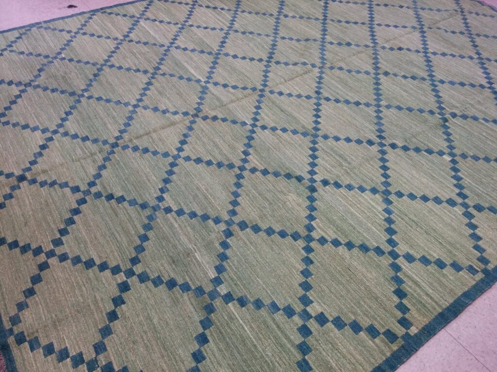 An overhead view of a green and blue geometric patterned rug, a product available from Yayla Tribal Rugs, Inc. in Cambridge, MA.
