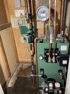 A green boiler unit with copper and black piping installed in a tight utility space by New Yorker Boiler in Lancaster, PA