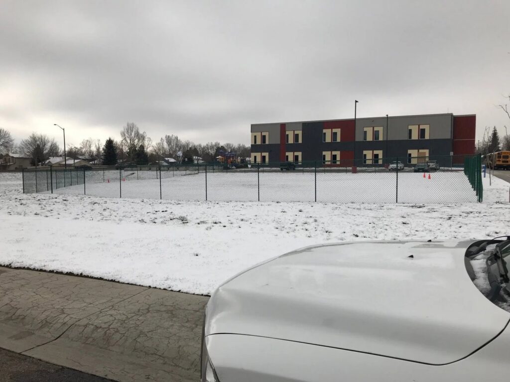 A green chain-link fence enclosing a small play area next to a school building, installed by Best Boy's Fencing in Fort Collins, CO.