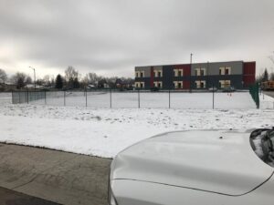 A green chain-link fence enclosing a small play area next to a school building, installed by Best Boy's Fencing in Fort Collins, CO.
