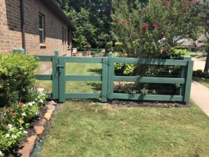 A green painted wooden fence with wire mesh and a gate, installed in a garden by GOAT Fence Company in Houston, TX.