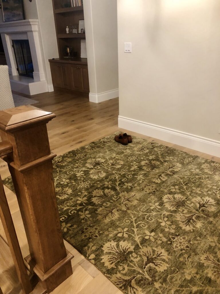 A beautiful green patterned area rug on a hardwood floor in a home, provided by Artifacts Fine Rugs and Flooring in South Salt Lake, UT.