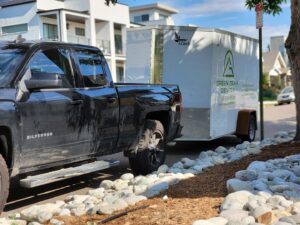 A Green Team Denver, CO, pickup truck towing an enclosed trailer with lawn care equipment.