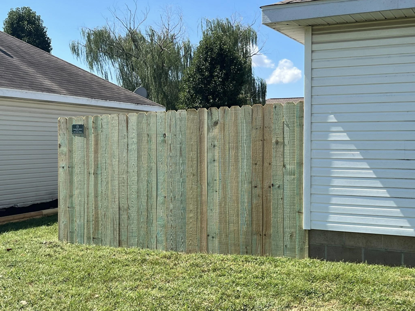 A section of newly installed green-treated wooden privacy fence in a residential yard by Timber Wolf Fence Co. in Rogers, AR.