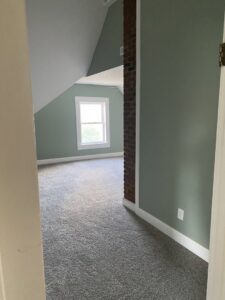 A bedroom with green walls and newly installed grey carpet by Carpet Warehouse in Lafayette, IN.